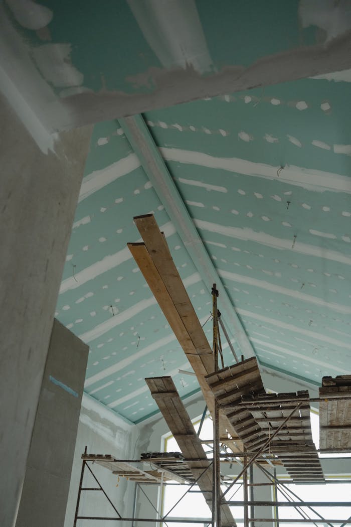 Scaffolding setup in an interior construction space with suspended ceiling boards and wooden planks.
